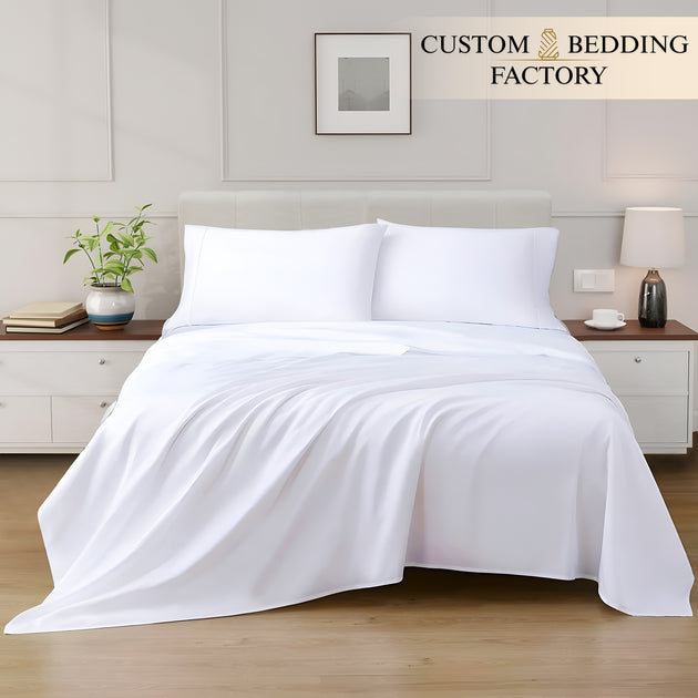 White bedding set on a bed in a bedroom with 'Custom Bedding Factory' branding.